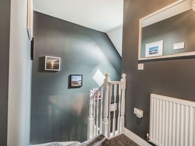 A stairway with white banisters and pictures on grey walls at Lantern House in Filey