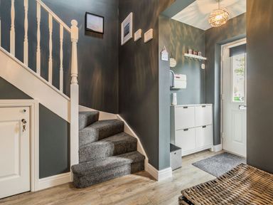 An entryway with carpeted stairs a white door a white cabinet and a wicker storage basket at Lantern House in Filey