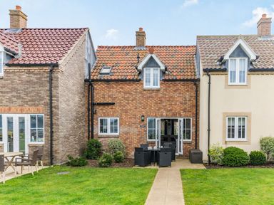 Backyard view of a brick house with outdoor dining set on a patio and green lawn at Lantern House in Filey