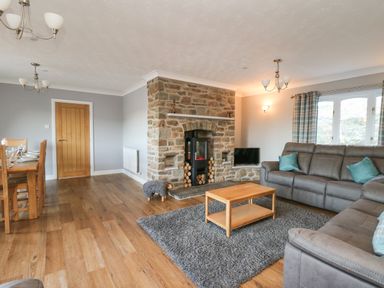 A living room with gray sofas wooden coffee table stone fireplace and dining table at Pen Y Banc in Llanfaredd near Builth Wells