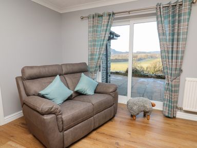 A living room with a brown sofa with teal cushions and plaid curtains near a glass door showing an outdoor view at Pen Y Banc in Llanfaredd near Builth Wells