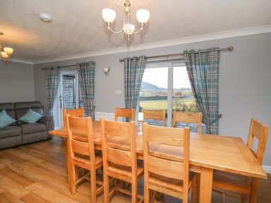 A dining room with a wooden table and chairs and a sofa with cushions near windows with plaid curtains at Pen Y Banc Llanfaredd near Builth Wells
