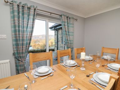 A dining room with a wooden table set for six and a sliding door with plaid curtains at Pen Y Banc Llanfaredd near Builth Wells