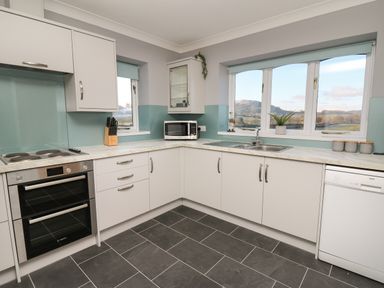 A kitchen with white cabinets oven microwave sink and dishwasher with windows overlooking hills at Pen Y Banc in Llanfaredd near Builth Wells