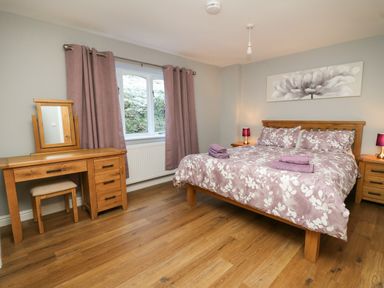 A bedroom with a wooden bed a floral bedspread wooden furniture and purple curtains at Pen Y Banc Llanfaredd near Builth Wells