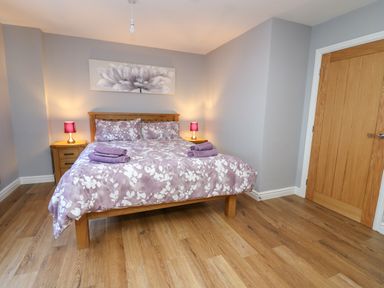 A bedroom with a wooden bed frame floral bedding two bedside tables with lamps wooden door and wooden floor at Pen Y Banc in Llanfaredd near Builth Wells