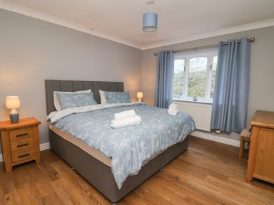A bedroom with a bed covered in blue bedding and white towels on top with wooden furniture and blue curtains at Pen Y Banc in Llanfaredd near Builth Wells