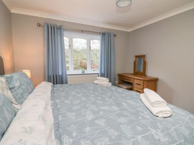 A bedroom with a bed covered in blue floral bedding next to a window with blue curtains and a wooden dressing table with a mirror at Pen Y Banc in Llanfaredd near Builth Wells