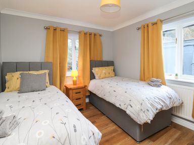 A bedroom with two single beds yellow curtains and a wooden nightstand with a lamp at Pen Y Banc Llanfaredd near Builth Wells