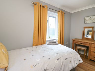 A bedroom with a bed with floral bedding near a window with yellow curtains and a wooden dressing table at Pen Y Banc in Llanfaredd near Builth Wells