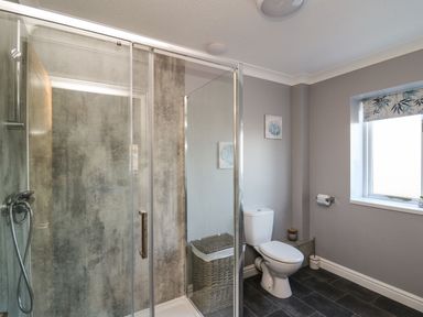 A bathroom with a glass shower enclosure a toilet a wicker laundry basket and a window at Pen Y Banc Llanfaredd near Builth Wells