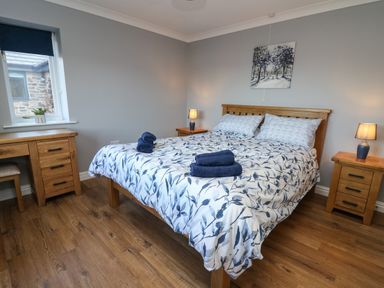 A bedroom with a bed covered in floral bedding two bedside tables with lamps a wooden desk and a window at Pen Y Banc in Llanfaredd near Builth Wells