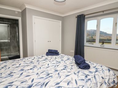 A bedroom with a bed with patterned bedding and folded towels near a window with dark curtains and a closet at Pen Y Banc in Llanfaredd near Builth Wells