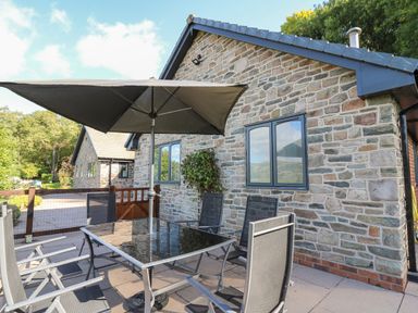 An outdoor patio with a glass table and chairs under a large umbrella next to a stone house at Pen Y Banc in Llanfaredd near Builth Wells