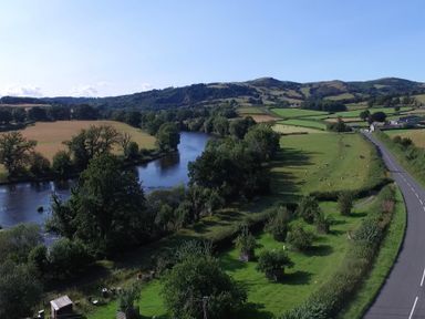 A river flowing through fields with trees and a road on the right side of the image at Pen Y Banc in Llanfaredd near Builth Wells