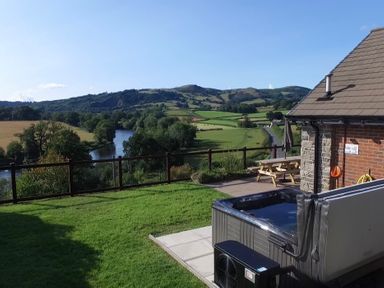 A garden with a hot tub a wooden picnic table and a river with hills in the background at Pen Y Banc in Llanfaredd near Builth Wells
