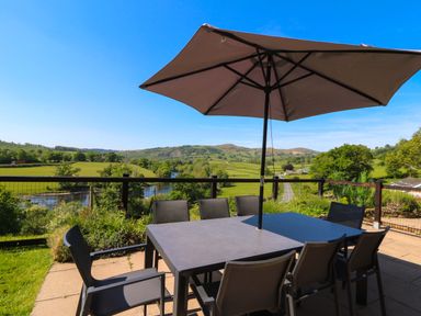 An outdoor patio table with chairs and an umbrella overlooking a river and green hills at Pen Y Banc in Llanfaredd near Builth Wells
