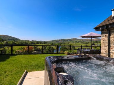 A backyard with a hot tub grass and outdoor dining table with umbrella overlooking hills and a river at Pen Y Banc in Llanfaredd near Builth Wells