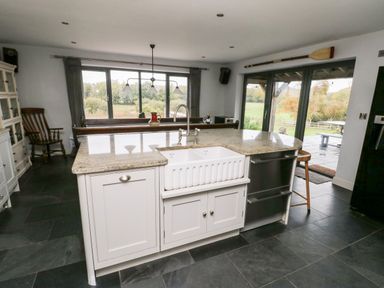 A kitchen island with a sink and faucet a wooden chair large windows and glass doors showing a garden outside at Cae Du in Dwyran near Niwbwrch Newborough