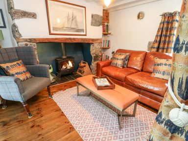 A living room with a fireplace a leather sofa an armchair and an orange bench at Cae Du in Dwyran near Niwbwrch Newborough