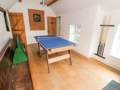 A room with a ping pong table wooden bench pool cues on the wall and a wooden floor at Cae Du in Dwyran near Niwbwrch Newborough
