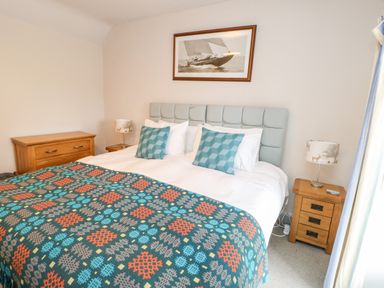 A bedroom with a bed a wooden dresser and bedside tables with lamps at Cae Du in Dwyran near Niwbwrch Newborough