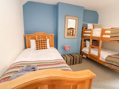 A bedroom with a single bed and bunk beds against blue and white walls at Cae Du in Dwyran near Niwbwrch Newborough