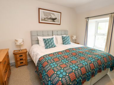 A bedroom with a bed headboard two bedside tables with lamps a framed picture above the bed and a window with curtains at Cae Du in Dwyran near Niwbwrch Newborough