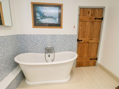 A bathroom with a freestanding bathtub blue tiled walls wooden door and a framed picture above the tub at Cae Du in Dwyran near Niwbwrch Newborough