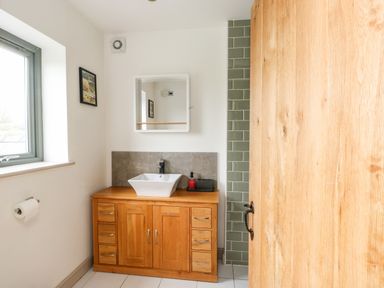 A bathroom with a wooden vanity cabinet and white sink under a mirror at Cae Du in Dwyran near Niwbwrch Newborough