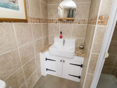 A bathroom sink with a mirror above and tiled walls at Cae Du in Dwyran near Niwbwrch Newborough