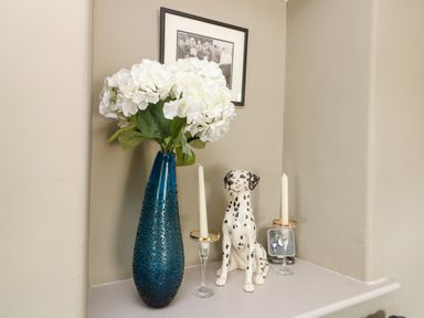 A shelf with a blue vase of white flowers a dalmatian figurine and two candlesticks at Cae Du in Dwyran near Niwbwrch Newborough