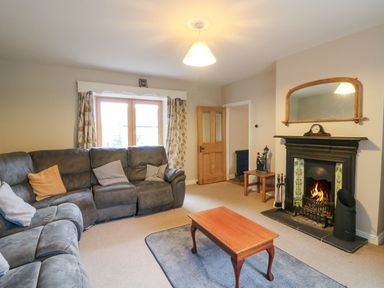 A living room with a gray sectional sofa a wooden coffee table a fireplace with a mirror above and a window with curtains at Coffey's Ballymacarbry County Waterford