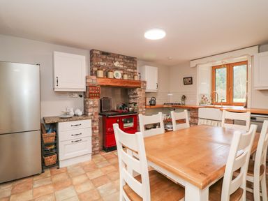 A kitchen with a wooden dining table and white chairs a red stove built into a brick fireplace and a window at Coffey's Ballymacarbry County Waterford
