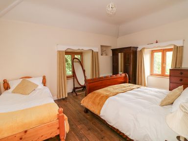 A bedroom with two beds a wooden floor a standing mirror an armoire and two windows at Coffey's Ballymacarbry County Waterford