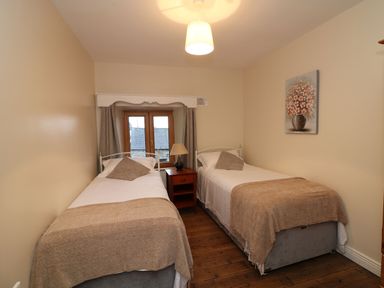A bedroom with two single beds a nightstand with a lamp between them a window with curtains and a painting of flowers on the wall at Coffey's Ballymacarbry County Waterford