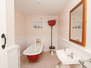 A bathroom with a red clawfoot bathtub a high-level toilet a white sink with taps and a wooden framed mirror at Coffey's Ballymacarbry County Waterford