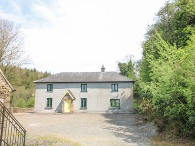 A detached house with a yellow front door and green window frames surrounded by trees at Coffey's in Ballymacarbry County Waterford
