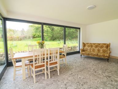 A dining area with a wooden table and chairs next to large windows and a patterned sofa in a room at Coffey's in Ballymacarbry County Waterford