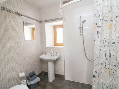A bathroom with a pedestal sink a mirror a window a shower with a curtain a small trash bin and tiled walls at Coffey's Ballymacarbry County Waterford