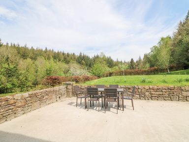 An outdoor patio with a table and six chairs surrounded by stone walls and greenery at Coffey's in Ballymacarbry County Waterford