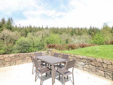 An outdoor patio with a table and six chairs surrounded by a stone wall and trees at Coffey's Ballymacarbry County Waterford