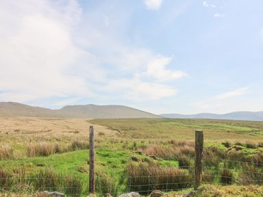 A grassy field with a wire fence and wooden posts with hills in the background at Coffey's in Ballymacarbry County Waterford
