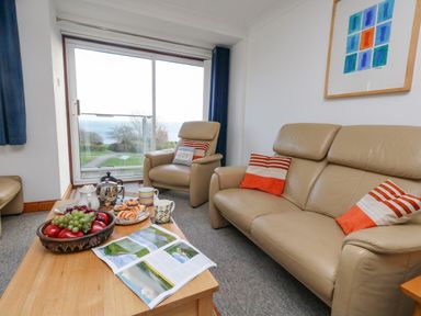 A living room with beige leather sofas and a wooden coffee table with fruit and tea set by a window with a sea view at Kiama in Weymouth