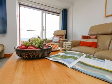 A living room with a wooden table holding a bowl of fruit a magazine and a cup in front of two leather armchairs with striped cushions at Kiama in Weymouth