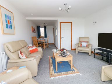 A living room with beige leather sofas a wooden coffee table and a dining area at Kiama in Weymouth