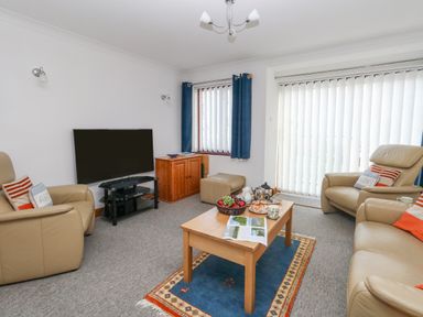 A living room with beige leather chairs a wooden coffee table with food a television on a stand and vertical blinds at Kiama in Weymouth