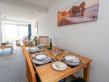 A dining table set with plates glasses and bread in a living room with armchairs and a large window at Kiama in Weymouth