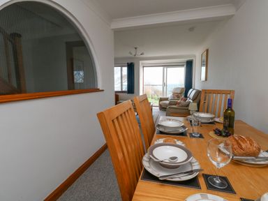 A dining table set with plates glasses and bread with a living area and sliding doors in the background at Kiama in Weymouth