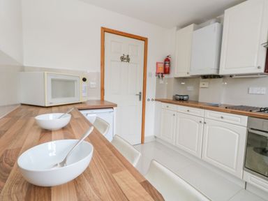 A kitchen with wooden countertops white cabinets a microwave a fire extinguisher and bowls with spoons at Kiama in Weymouth